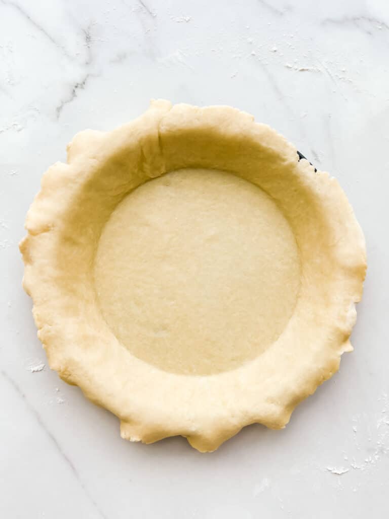 A pie plate lined with pie dough, ready to be filled with fruit to make a pie.