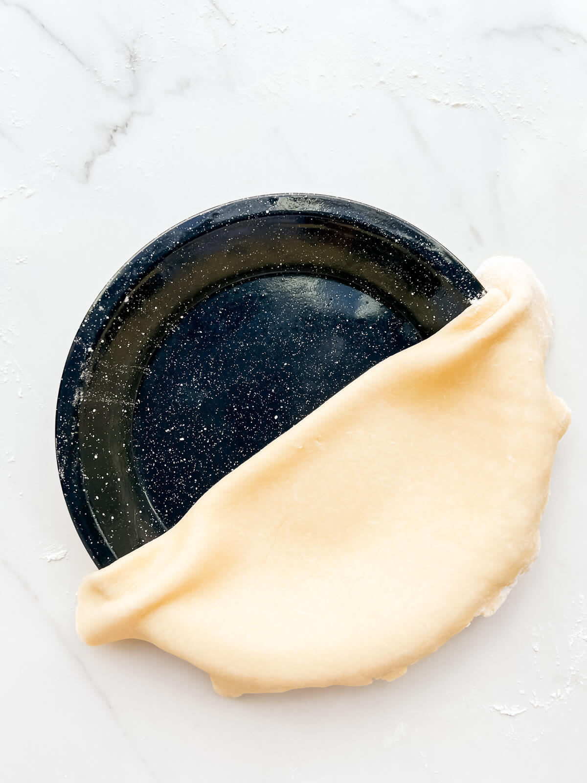 Lining a pie plate with pie dough, unfolding the dough across the surface of the plate.