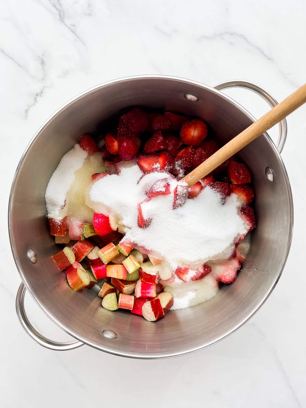 Mixing strawberries and rhubarb with sugar and lemon juice in a pot to macerate and then make homemade jam.