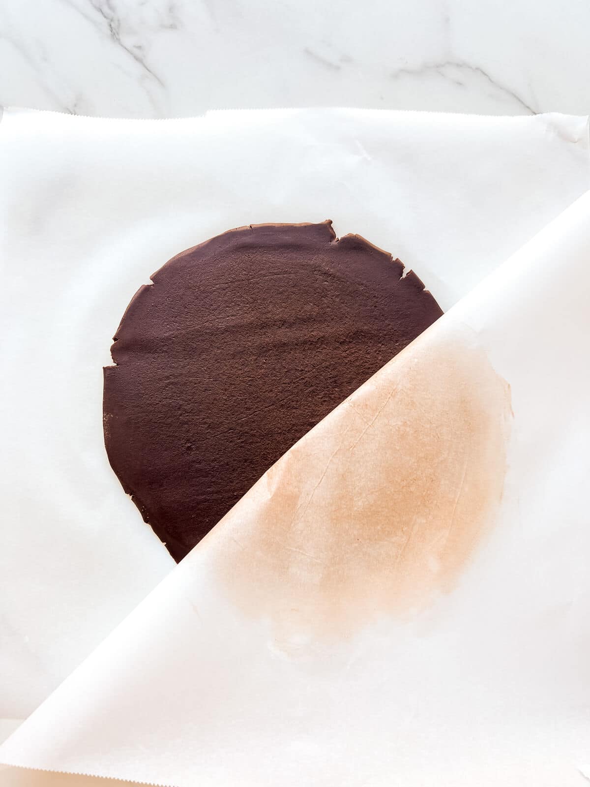 Rolled out chocolate dough between two sheets of parchment paper to make cutout cookies.