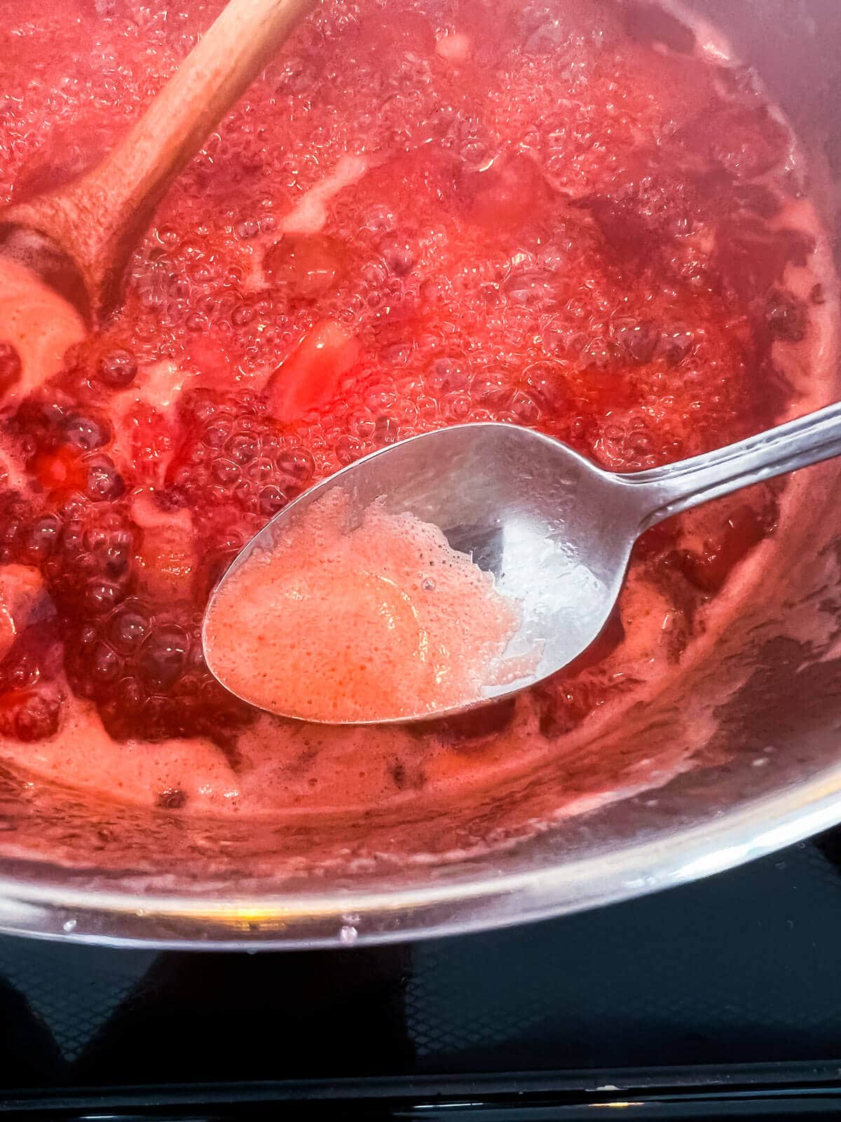 Skimming foam off of the surface of boiling jam to produce a more clear jam without any foam or bubbles.