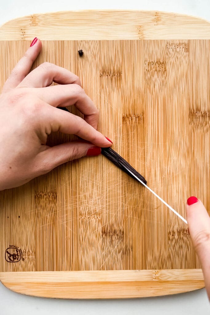 Splitting a vanilla bean in half lengthwise to open up the pod so you can scrape the caviar out with a pairing knife.