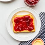 Strawberry jam with rhubarb smeared on a piece of toast on a plate.