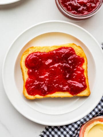 Strawberry jam with rhubarb smeared on a piece of toast on a plate.