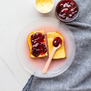 Toast served with homemade strawberry jam and butter on a pink plate.