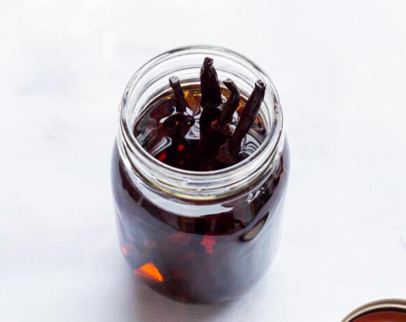 An open jar of homemade vanilla extract with vanilla beans poking up above the alcohol.