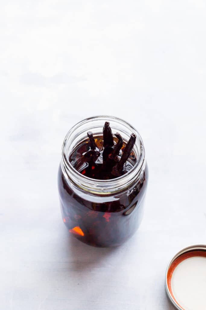 An open jar of homemade vanilla extract with vanilla beans poking up above the alcohol.