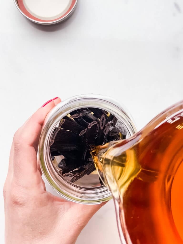 Pouring alcohol over vanilla beans in a jar to make homemade extract.