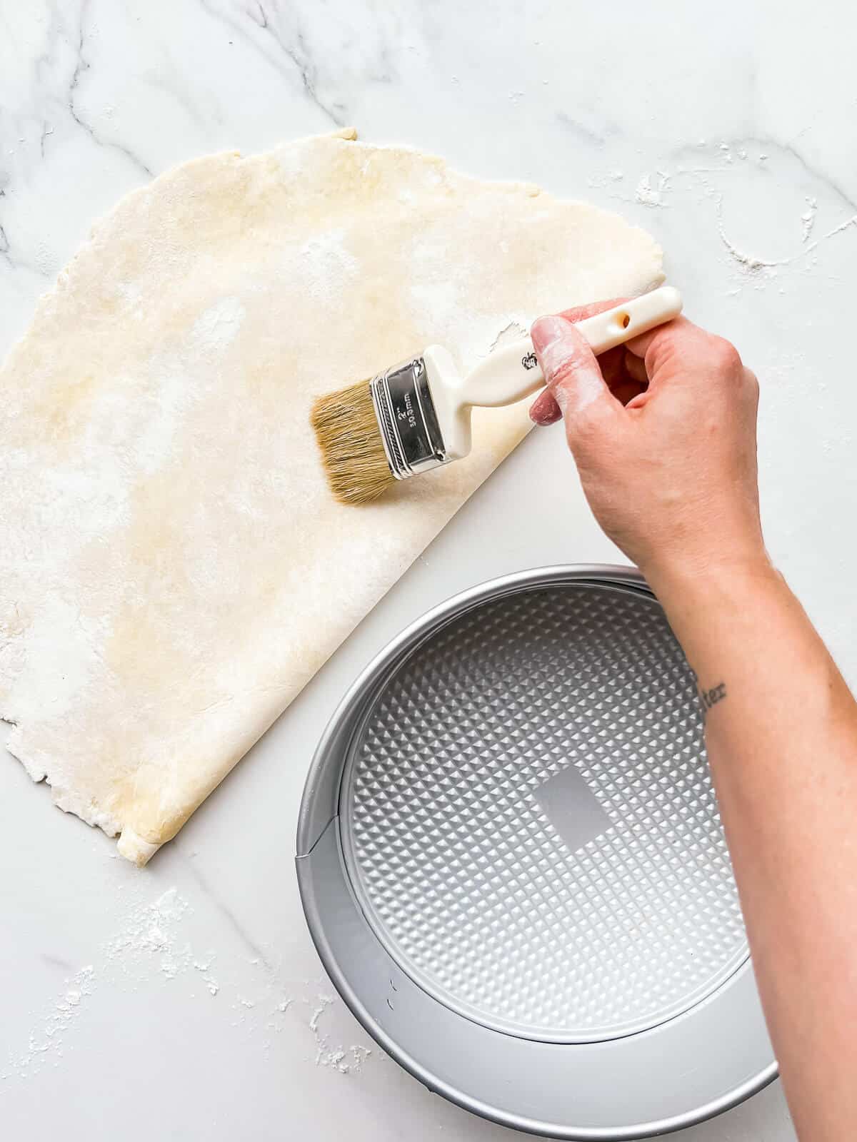 Brushing excess flour off of pie crust before transferring it to a pan.