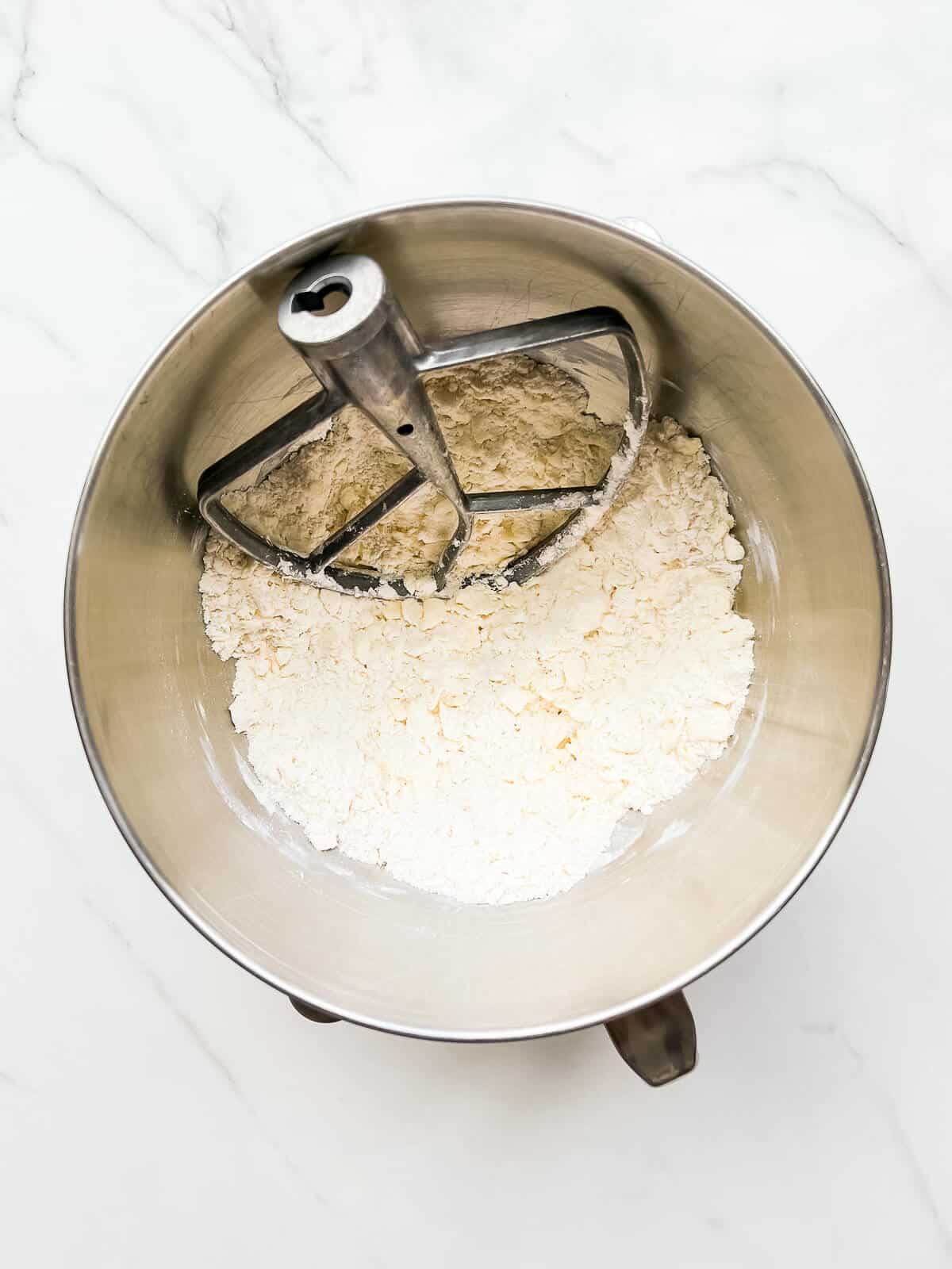 Stand mixer bowl with paddle attachment, as well as dry ingredients with butter worked in to make a shaggy mixture.