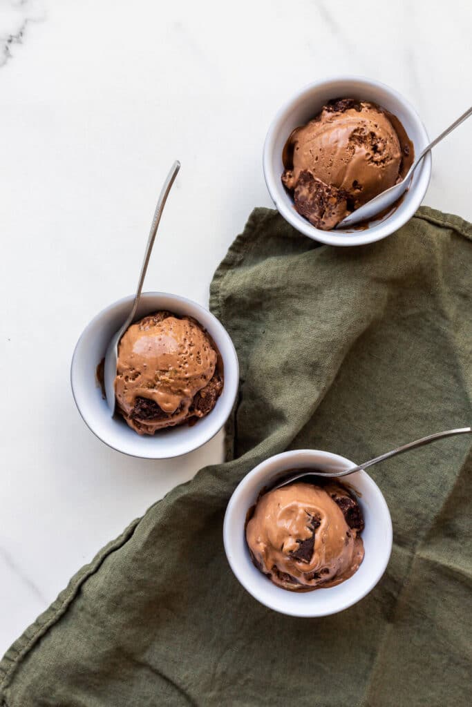 Chocolate brownie ice cream scooped into three small grey bowls with spoons.