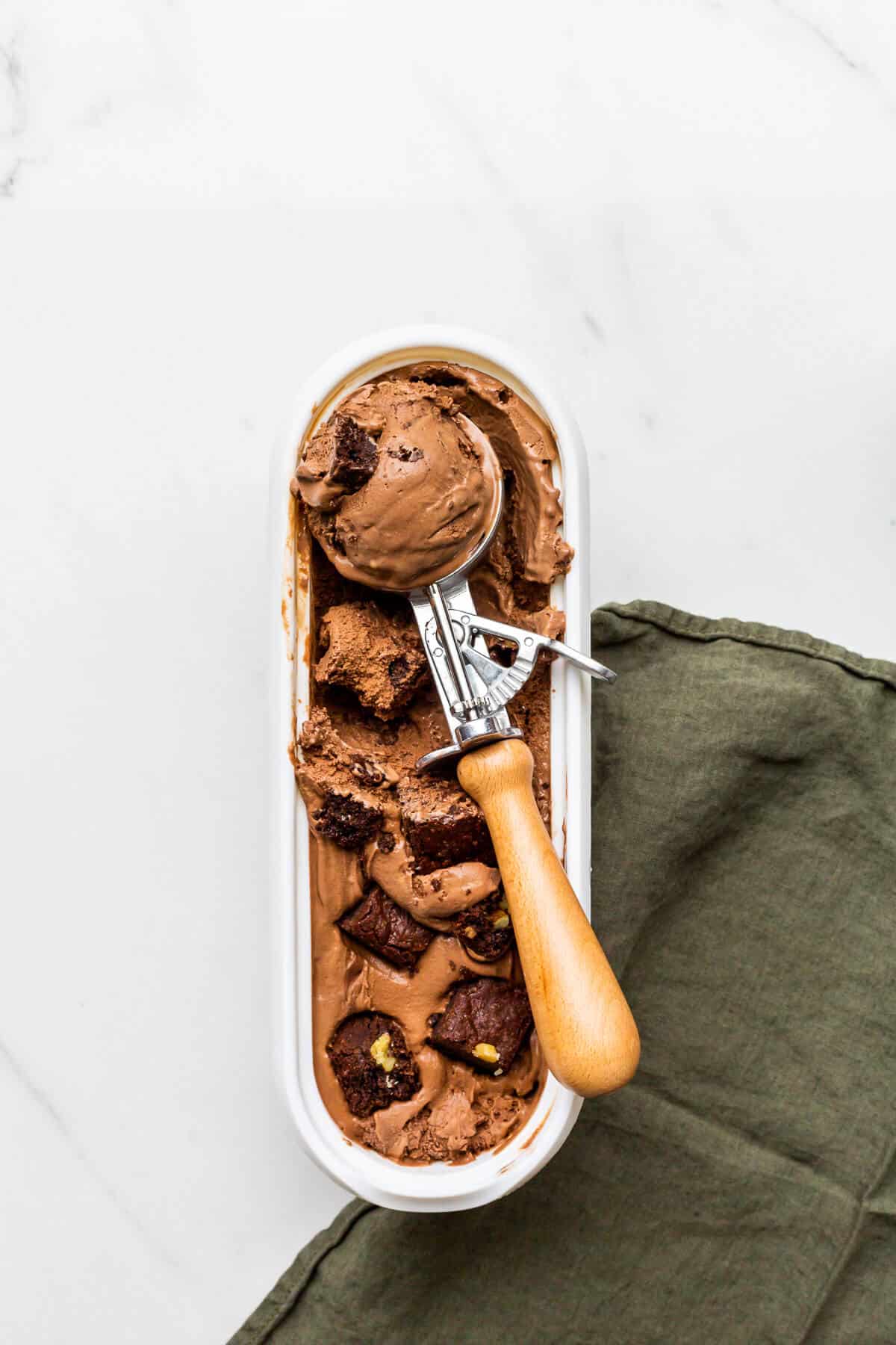 Scooping chocolate brownie ice cream with an ice cream scoop from a big tub.