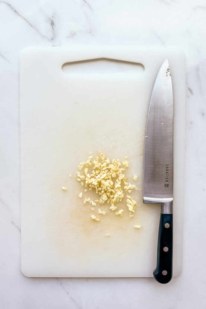 Chopping garlic on a white cutting board with a Chef knife.