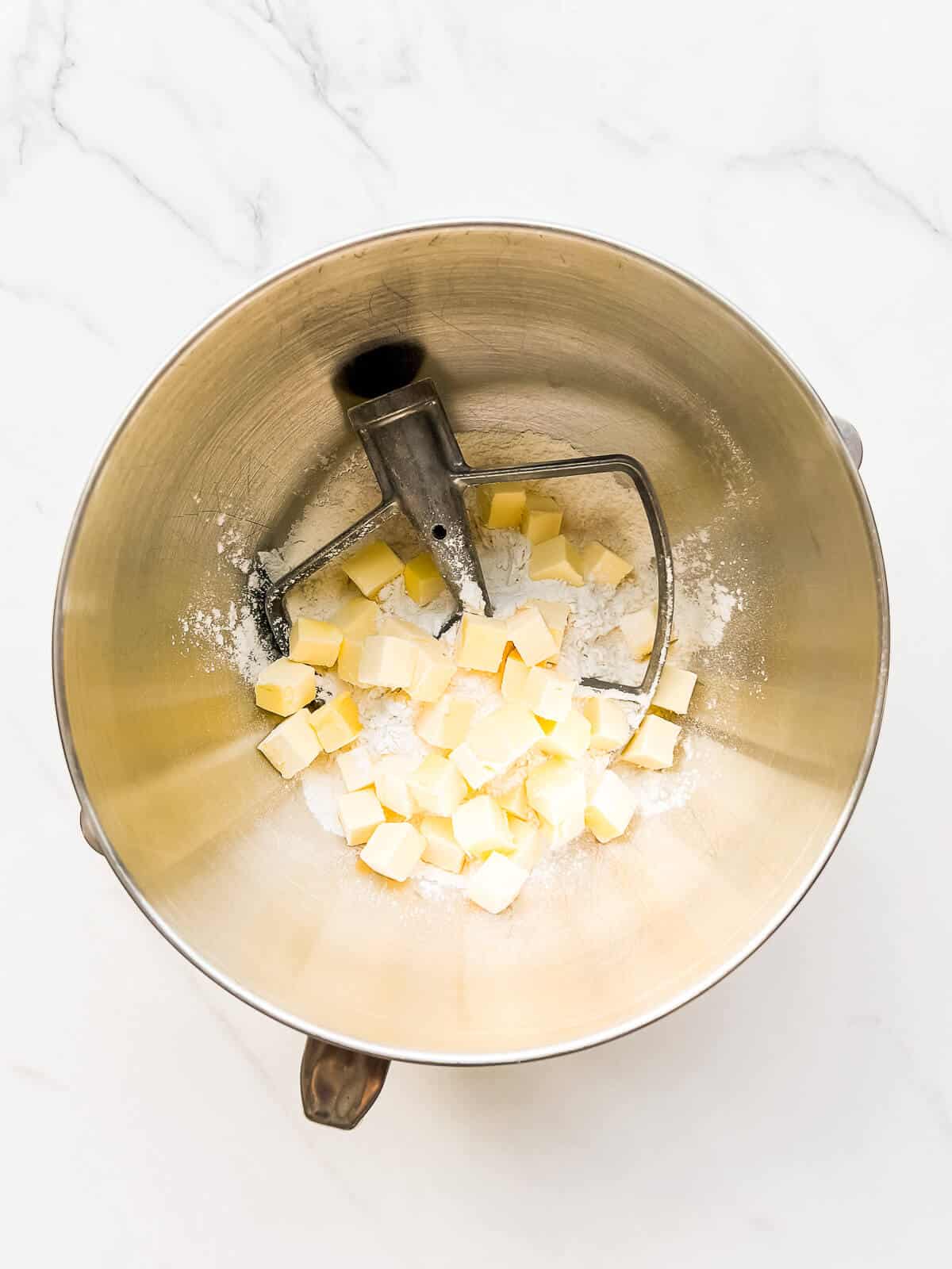 Stand mixer bowl with paddle attachment, as well as dry ingredients with cubes of cold butter.