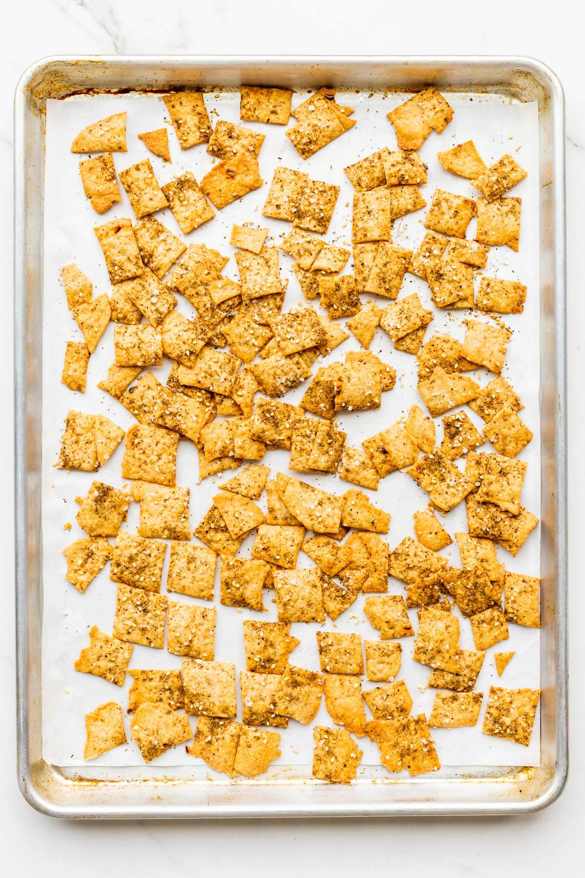 A sheet pan of golden brown baked crackers topped with salt, spices and sesame seeds.