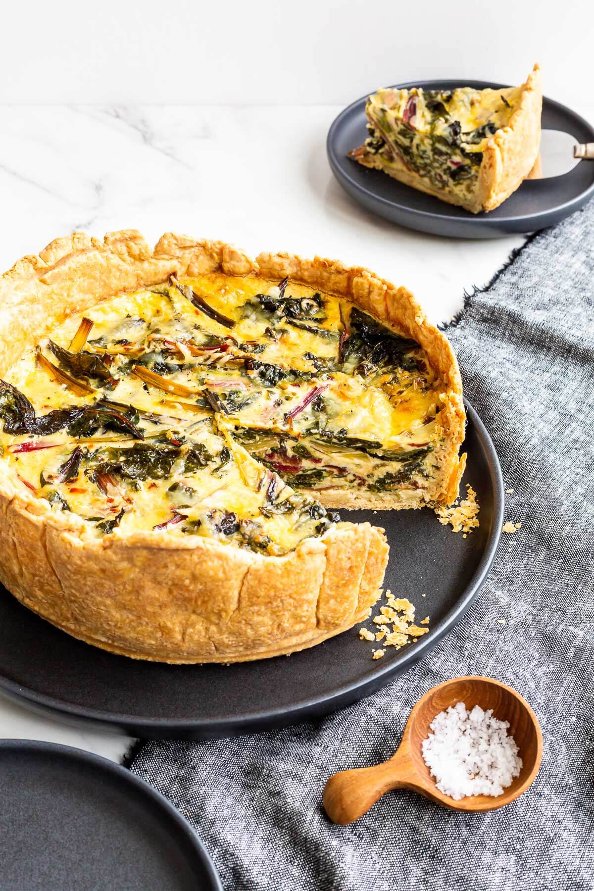 A deep dish quiche with a slice removed to a plate in the background.