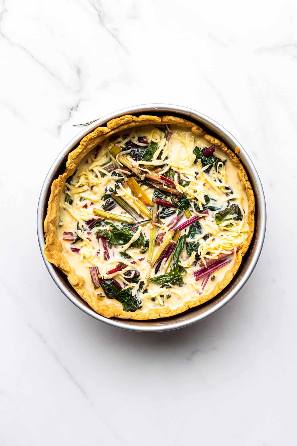 A blind baked pie crust in a 9 inch springform pan filled with a savoury custard, Swiss chard, and shredded cheese, ready to be baked.