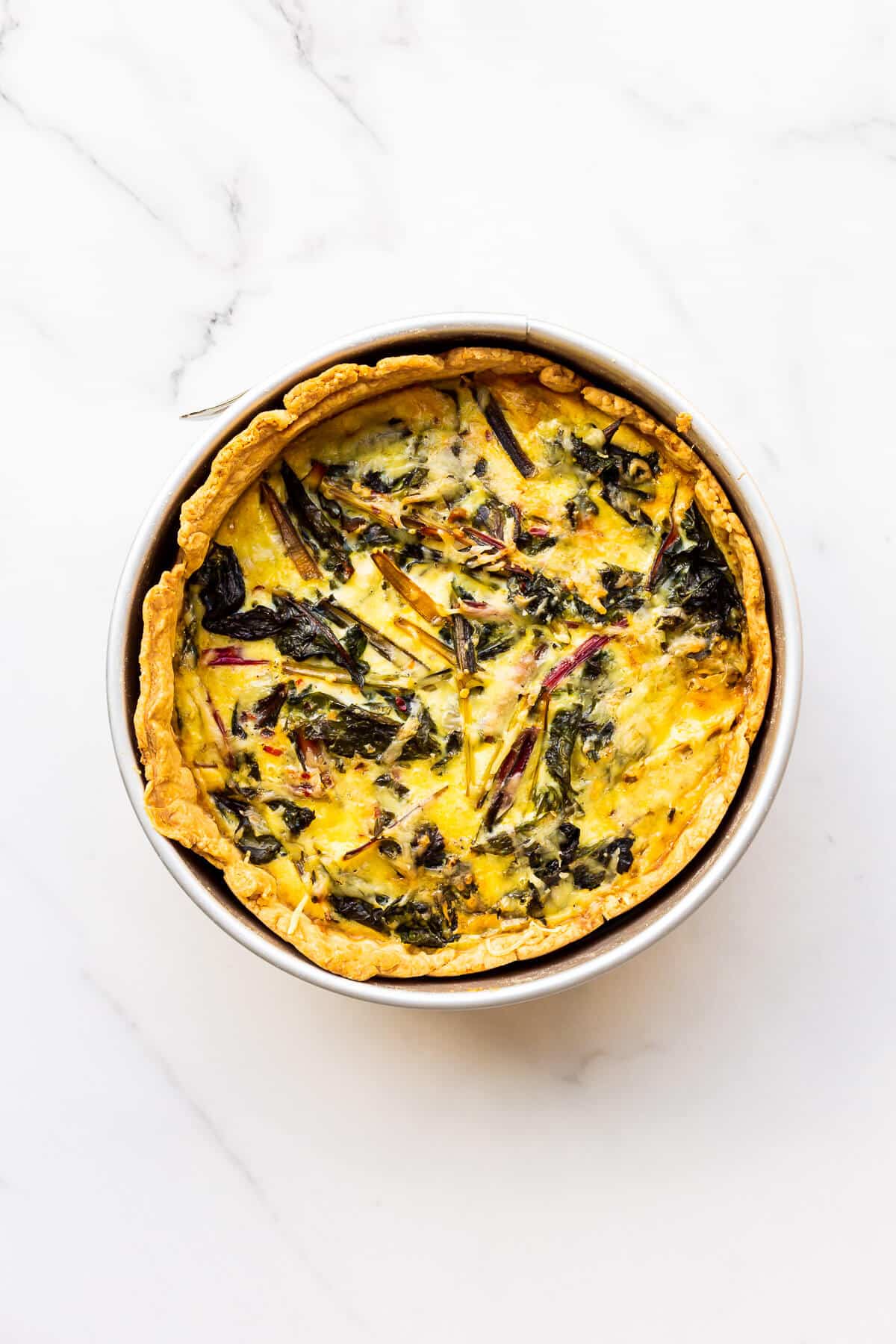 A deep dish quiche baked in a springform pan with cheese and rainbow Swiss chard.