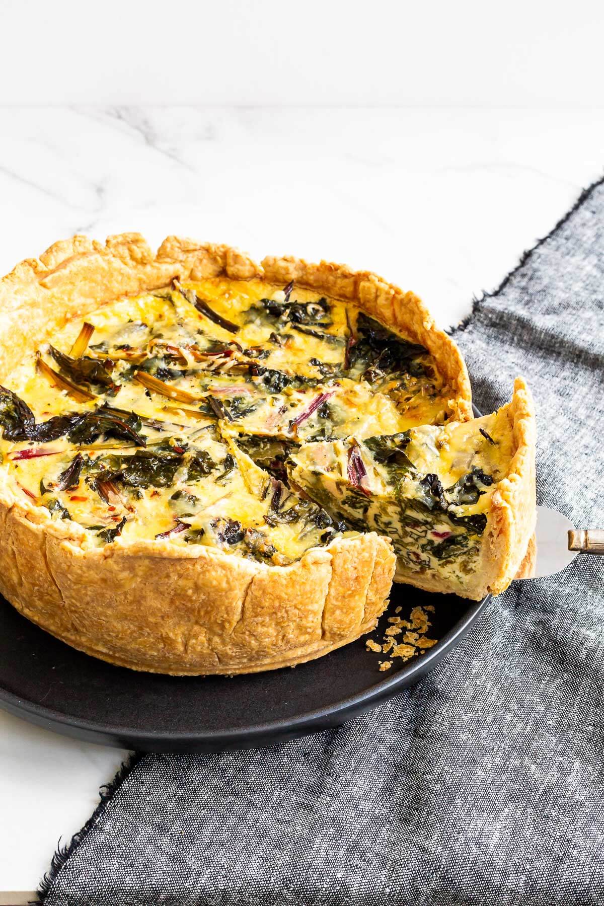 Removing a slice of deep dish quiche to show the layers of Swiss chard inside.