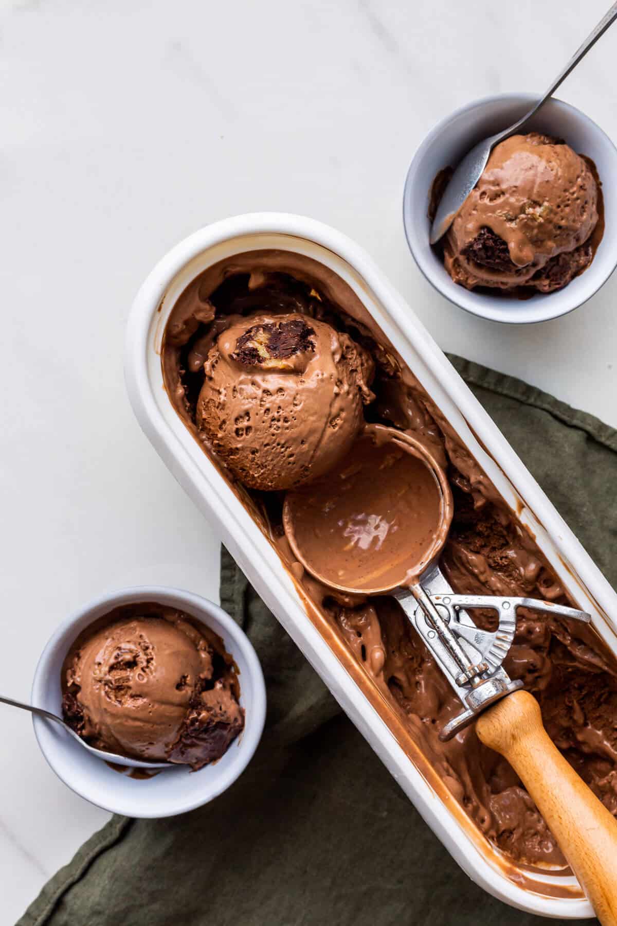 Scooping chocolate brownie ice cream with an ice cream scoop into small bowls.