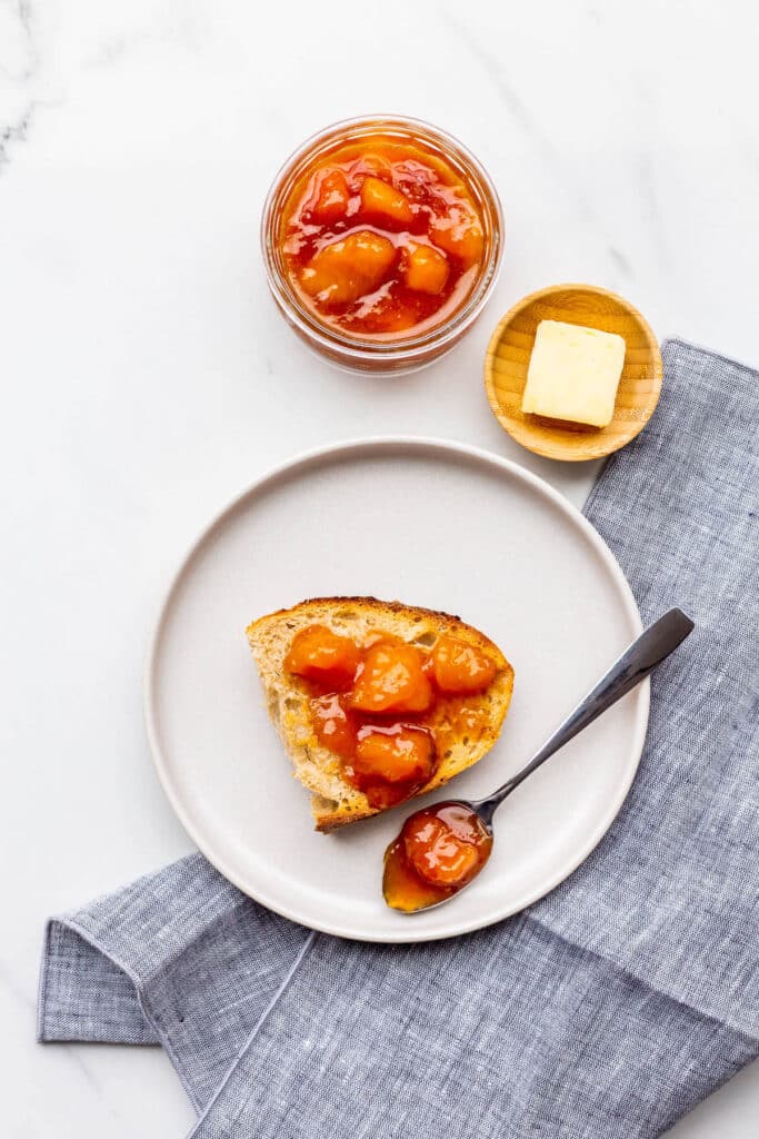 A piece of sourdough bread with peach jam spooned on top.