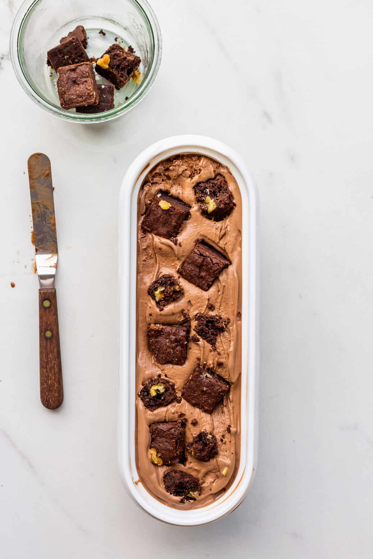 Layering brownie pieces over soft chocolate ice cream to make chocolate brownie ice cream.