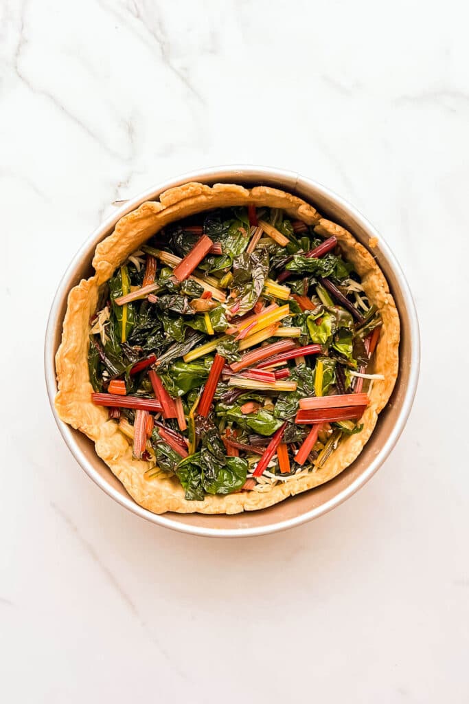 Layering sautéed rainbow Swiss chard in a blind-baked crust to make a quiche.