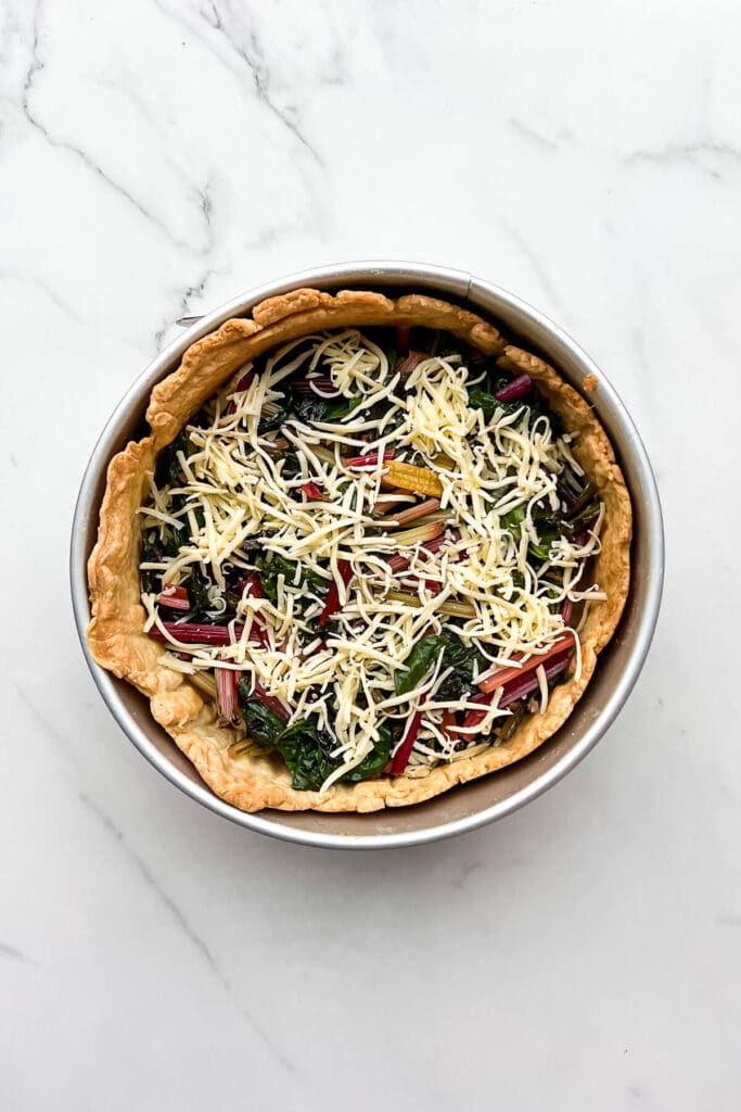 Layering sautéed rainbow Swiss chard and cheese in a blind-baked crust to make a quiche.