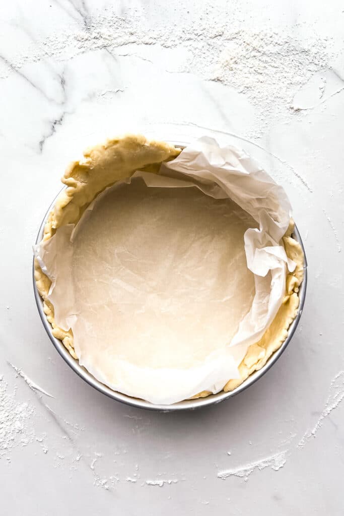 An unbaked pie crust in a springform pan with parchment paper on top for blind-baking.