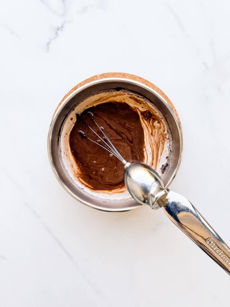 Whisking dark chocolate into hot cream and cocoa powder to make an ice cream base.