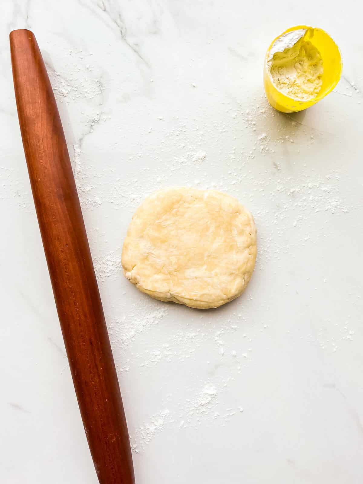 A disk of chilled pie dough to be rolled out with a tapered French rolling pin on a floured surface.