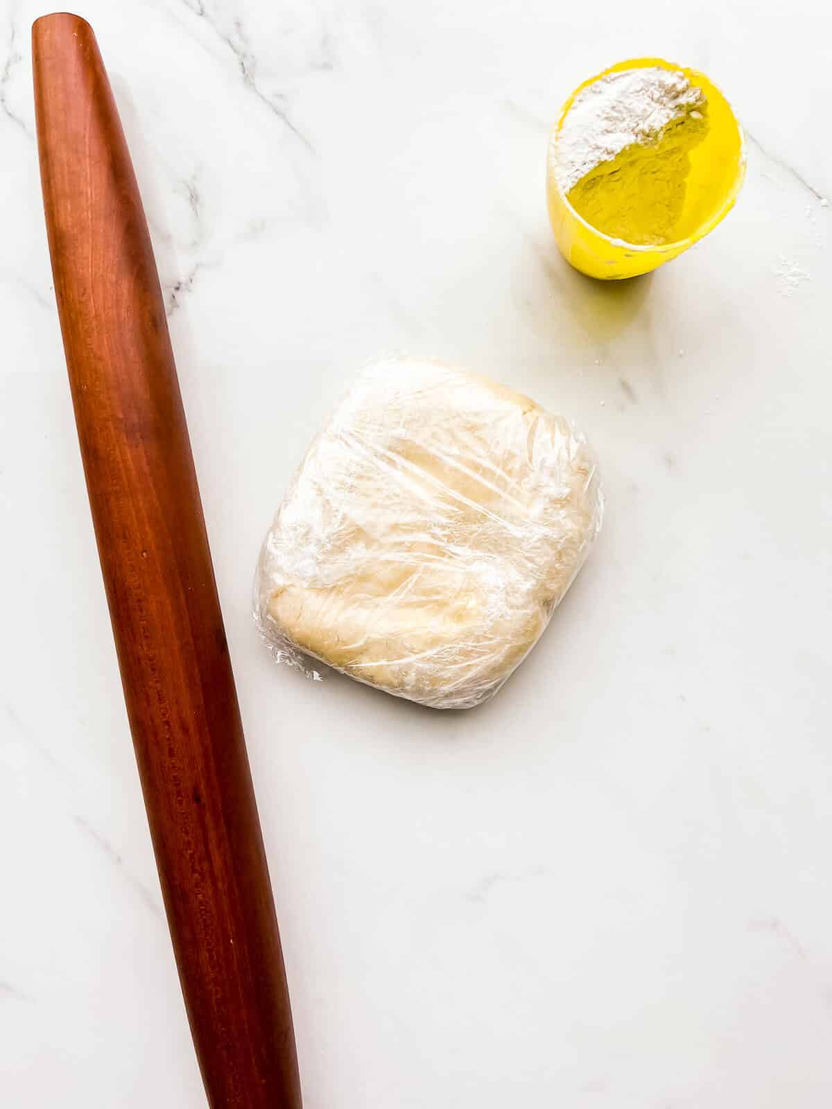 A wrapped disk of pie dough to be rolled out with a French rolling pin with flour to prevent sticking.