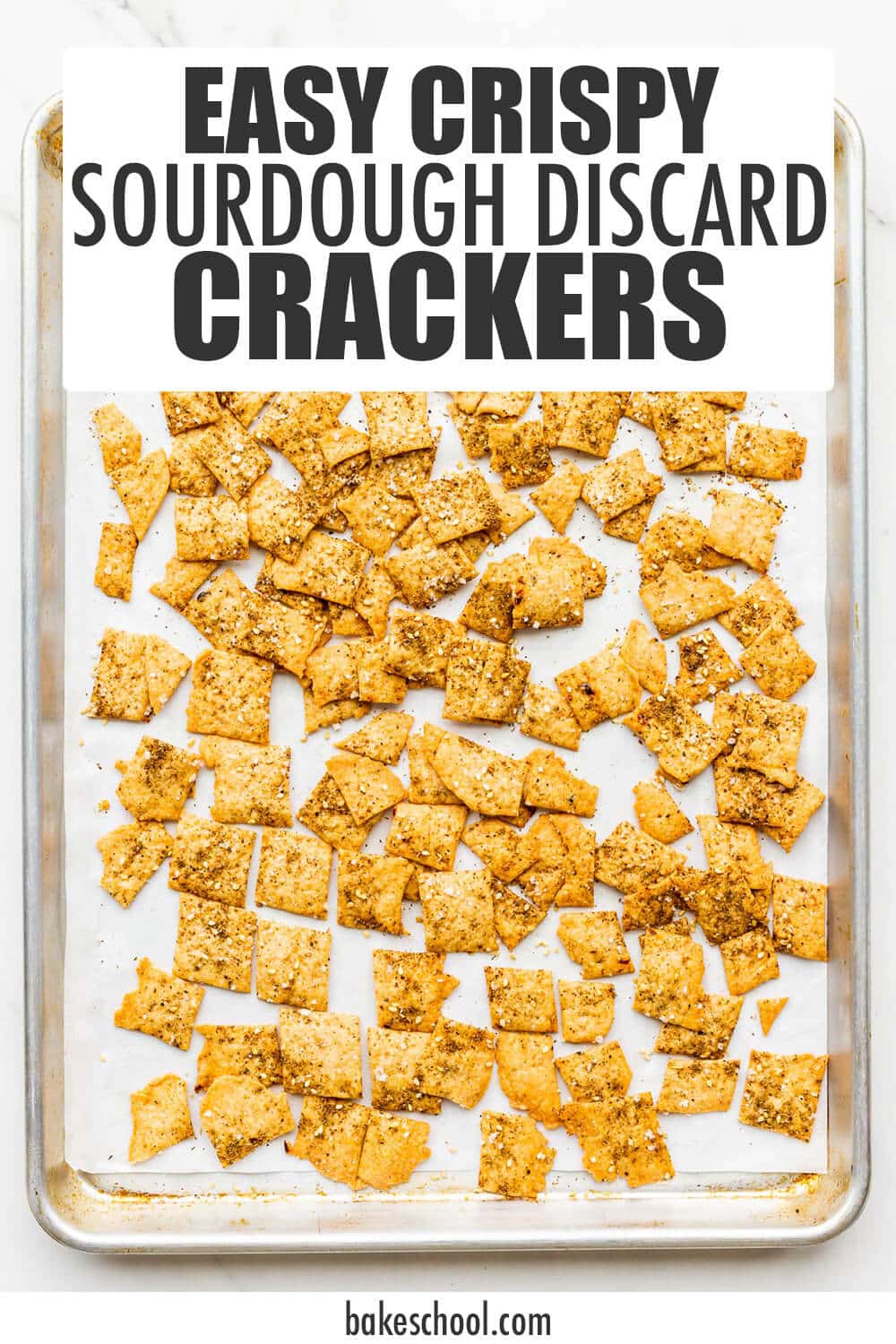 A sheet pan of golden brown baked crackers topped with salt, spices and sesame seeds.