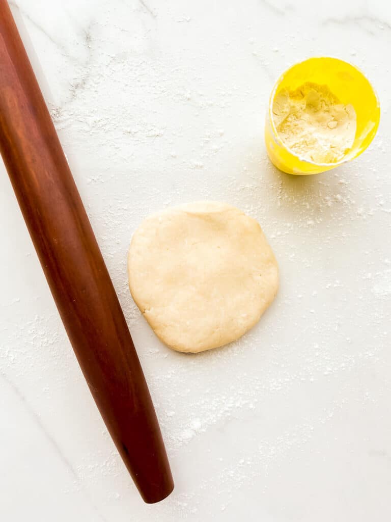 Pie dough and a French rolling pin on a floured surface, ready to be rolled out into a round, thin sheet to make a pie crust.