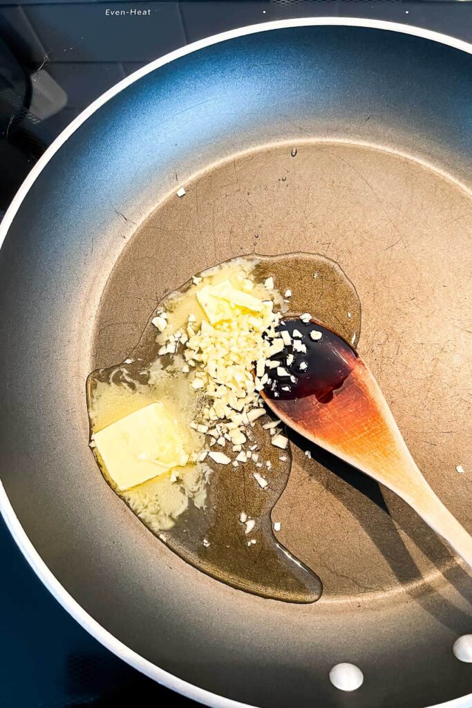 Sautéeing chopped garlic in butter and olive oil in a non-stick fry pan with a wooden spoon.