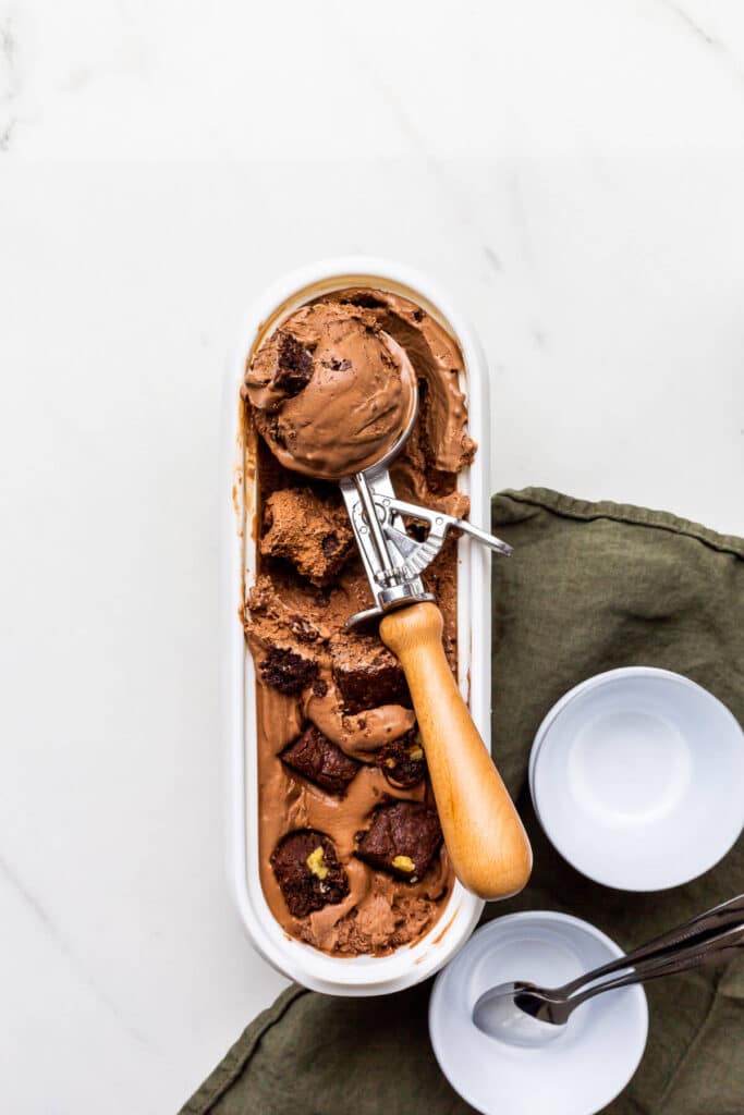 Scooping chocolate brownie ice cream with an ice cream scoop into small bowls.