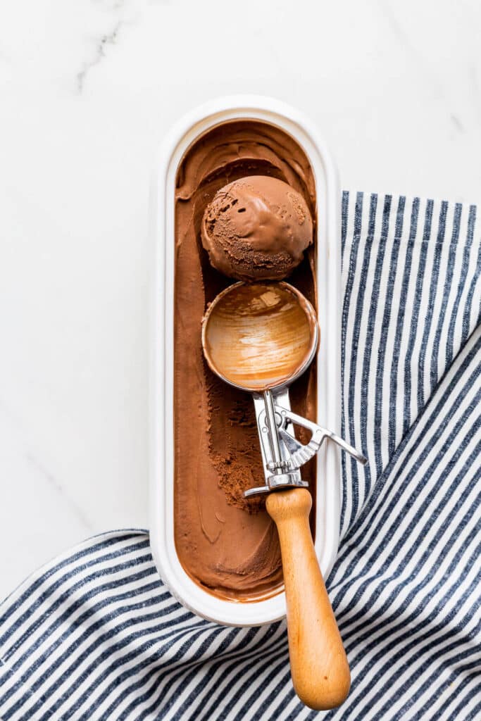 Scooping homemade chocolate ice cream from a tub with an ice cream scoop.