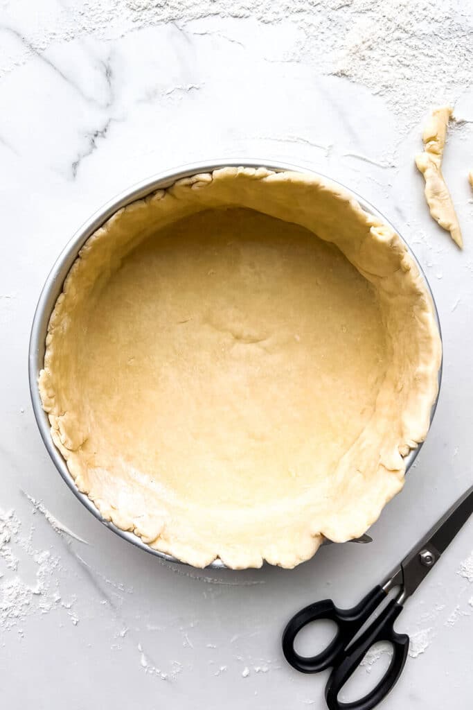 A springform pan lined with pie dough and a pair of scissors to trim the excess before blind baking it.