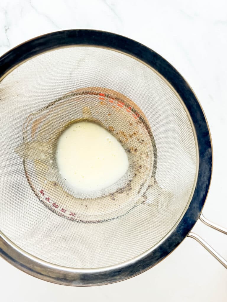 Straining crème anglaise into a large measuring with a chocolate base to make ice cream.