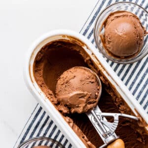 Scooping chocolate ice cream with an ice cream scoop into glass bowls.