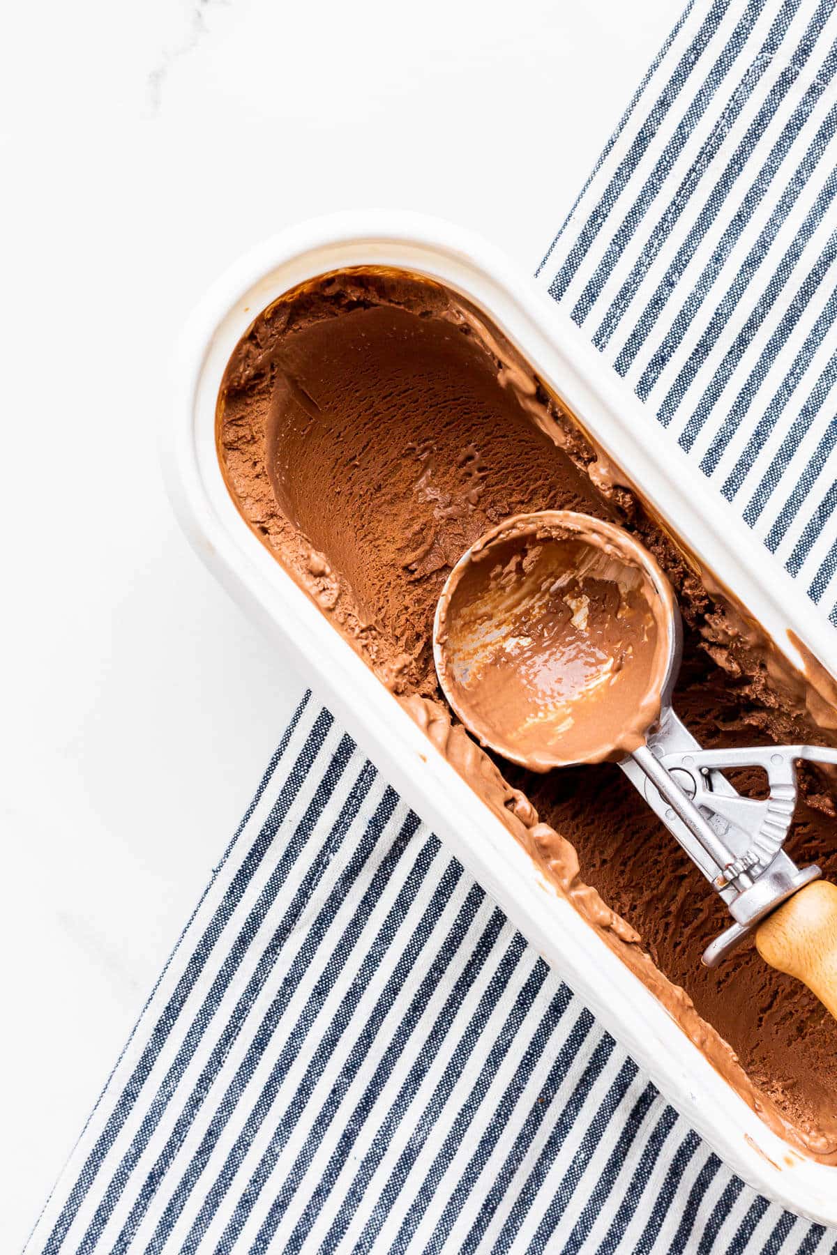 A tub of chocolate ice cream with an ice cream scoop with a wood handle.