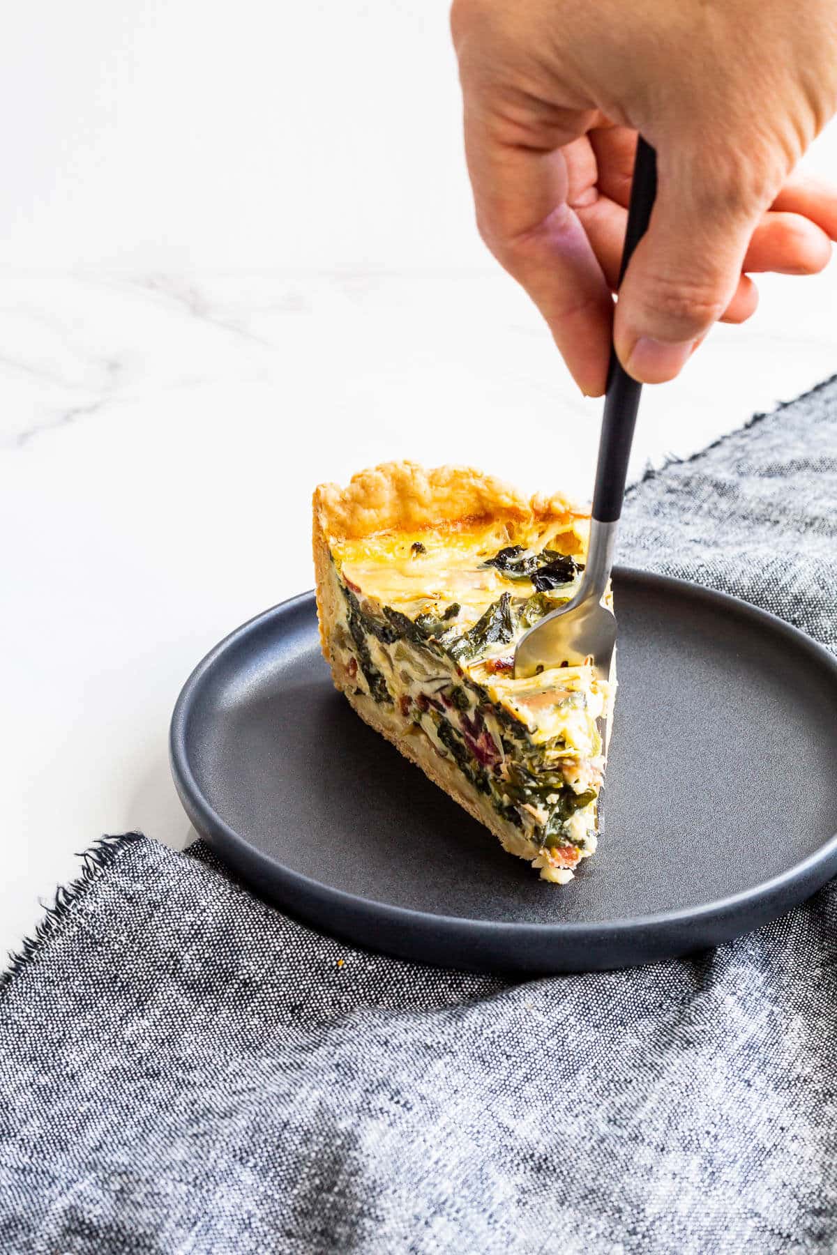 A slice of homemade quiche on a black plate with a fork in it.