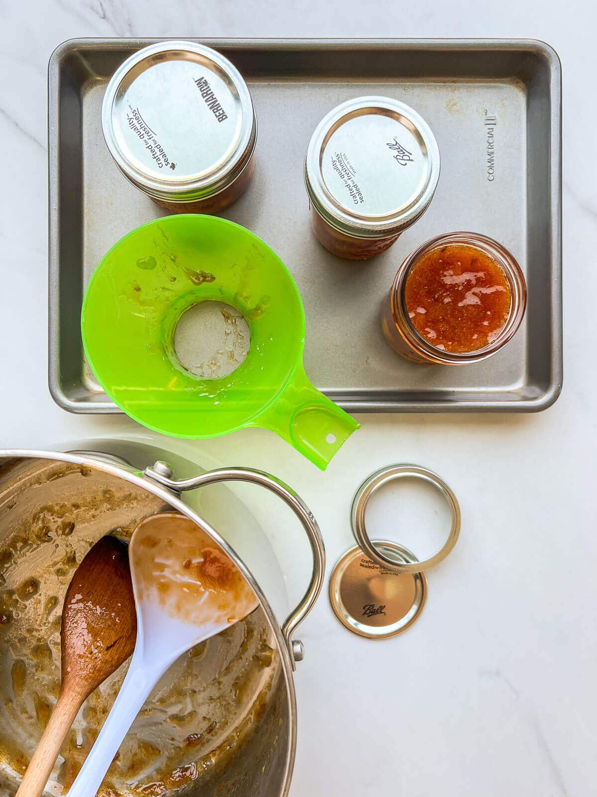 Transferring peach jam to jars with a ladle before sealing them shut to preserve the jam.