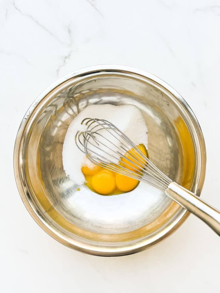 Whisking egg yolks and sugar in a bowl before tempering them to make a crème anglaise for ice cream.