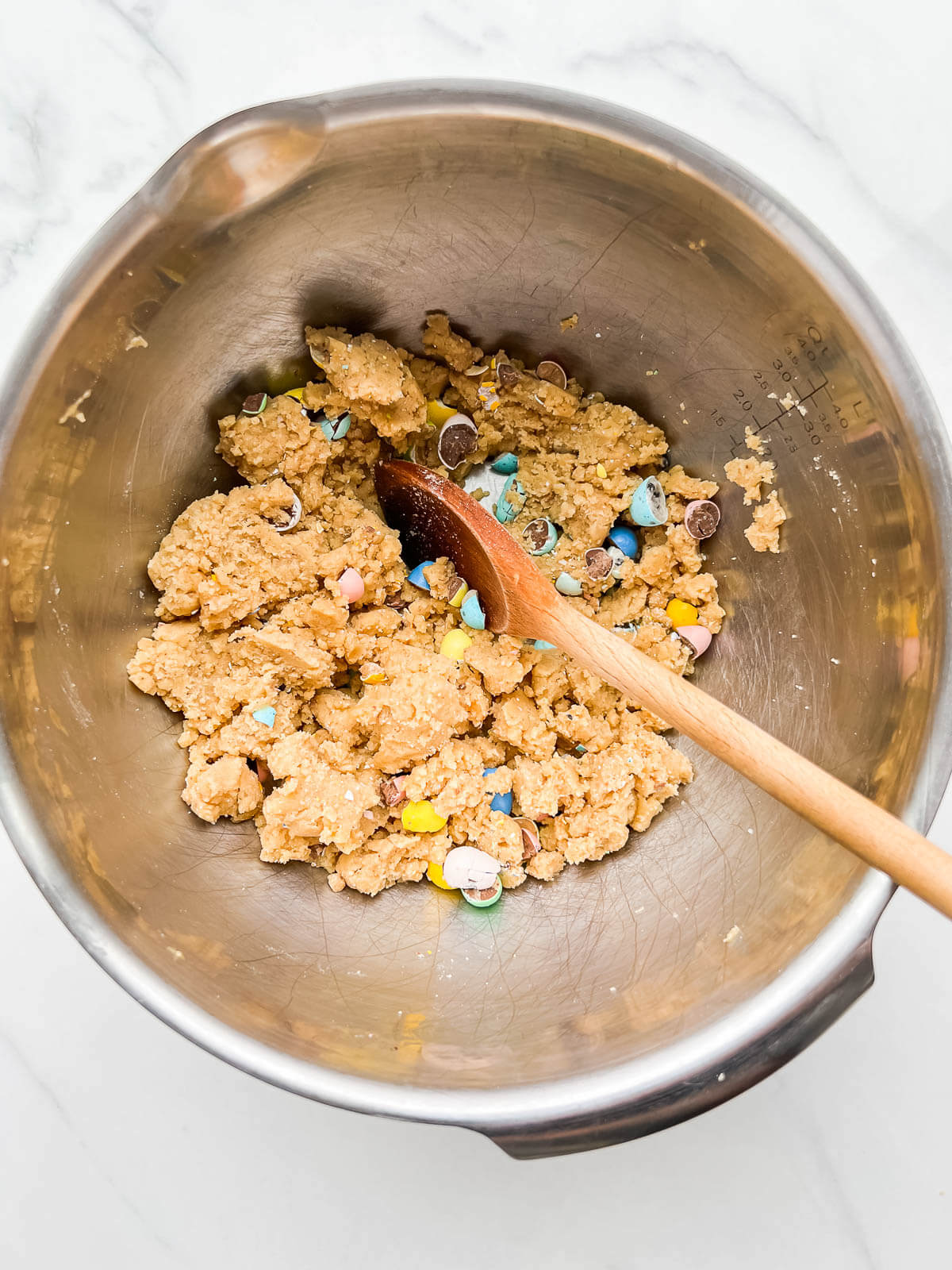 Stirring Mini Eggs into cookie dough in a stainless steel bowl to make Easter blondies.