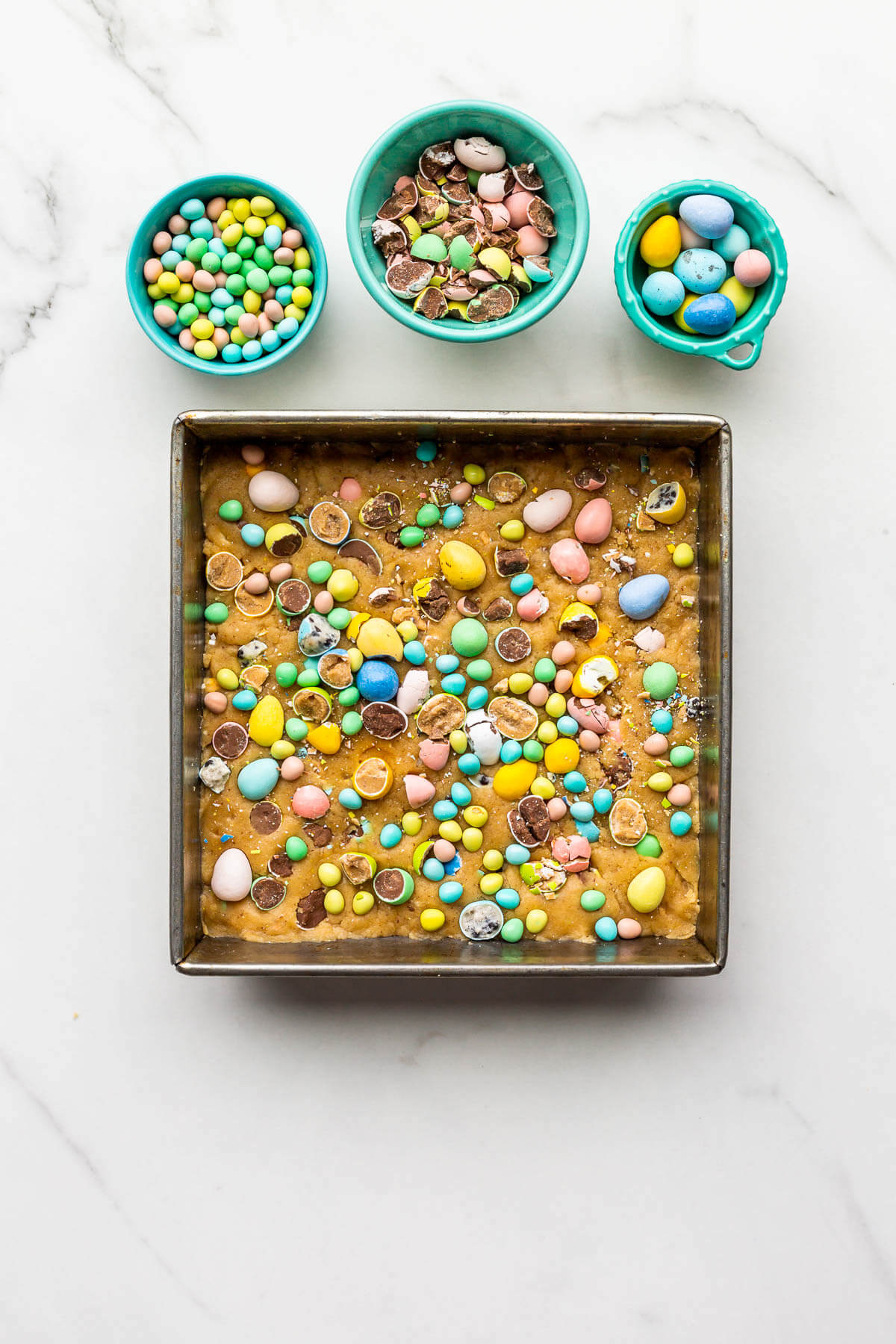 Scattering chopped Easter Mini Eggs on the surface of a pan of blondies before baking them in the oven.