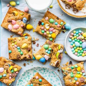 Mini Egg bars cut into squares and served on small plates with a glass of milk on the side and a bowl of Mini Eggs.