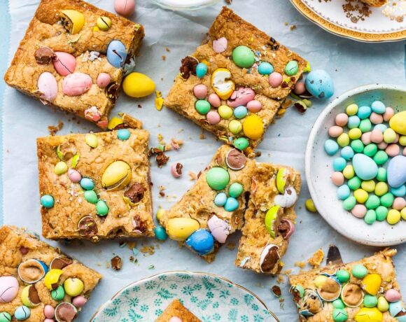 Mini Egg bars cut into squares and served on small plates with a glass of milk on the side and a bowl of Mini Eggs.