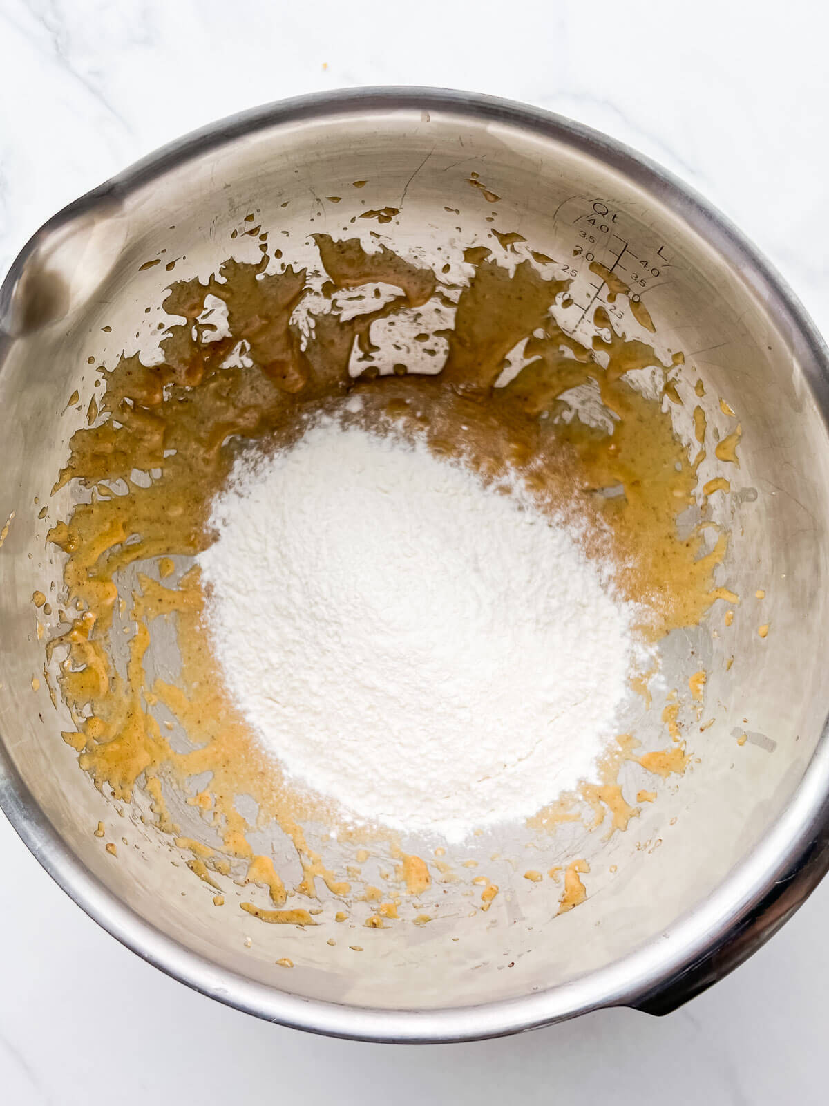 Dry ingredients sprinkled over creamed butter, sugar, and eggs in a stainless steel bowl to make blondies or cookie bars.