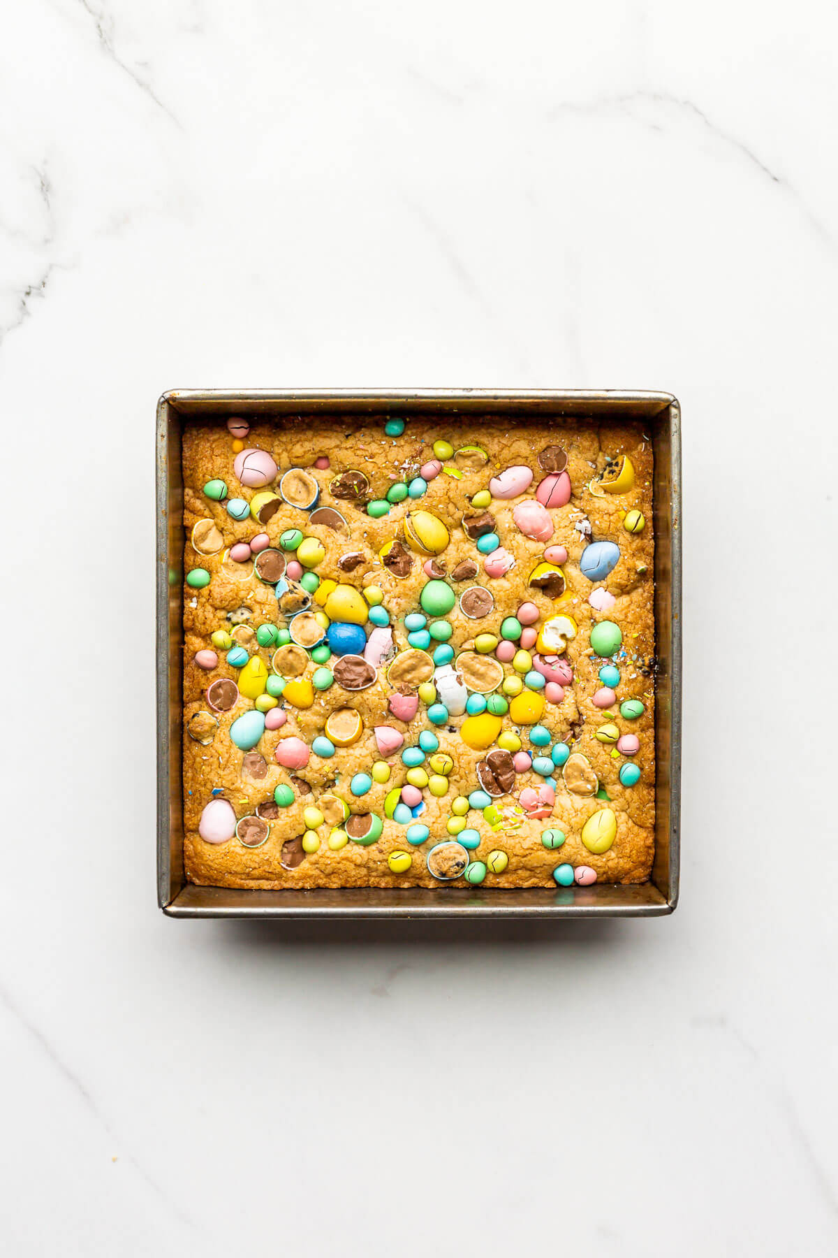 A pan of freshly baked Mini Egg cookie bars set on a marble surface to cool.